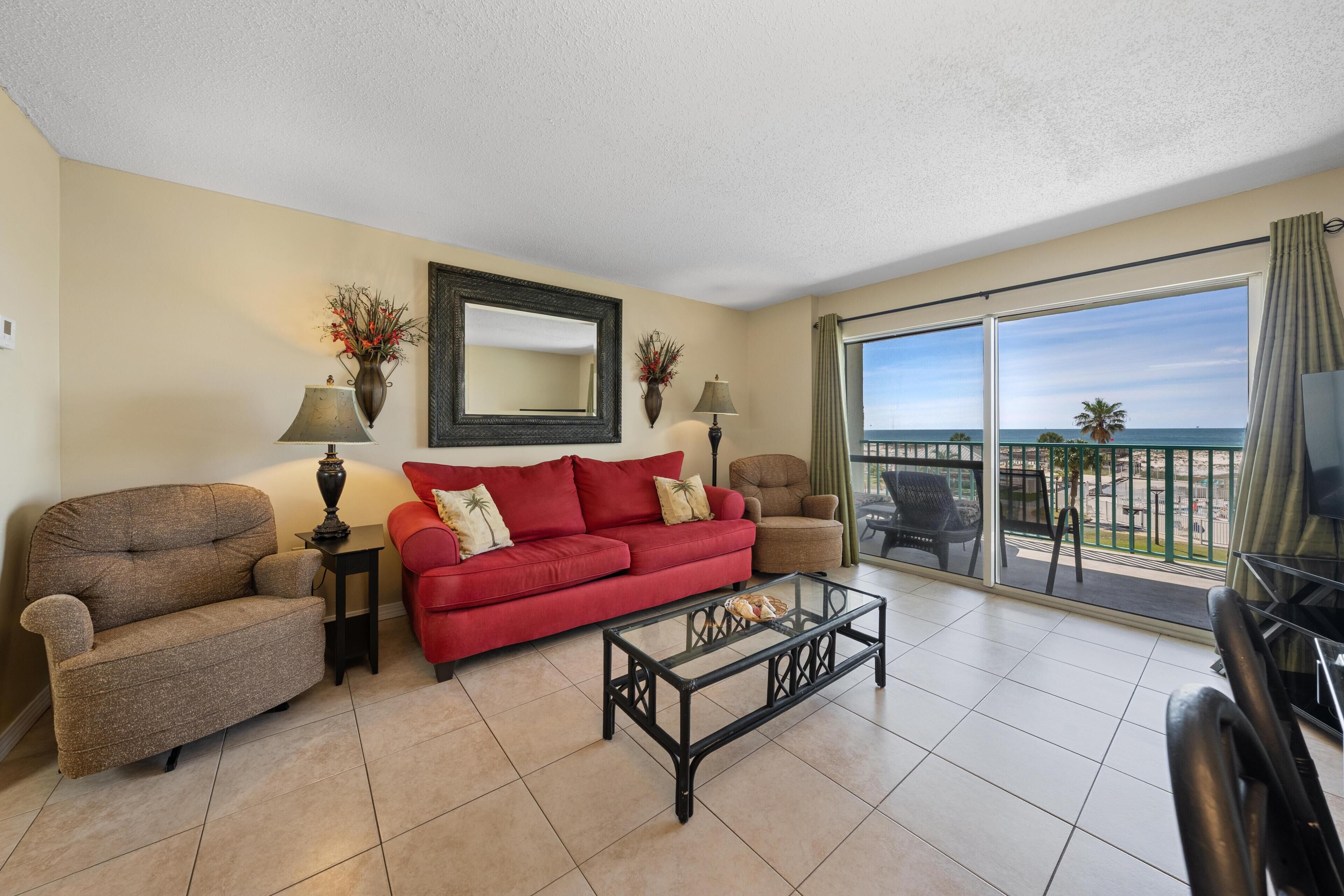 A living room with a red sofa, two armchairs, a coffee table, and a large window with a view.