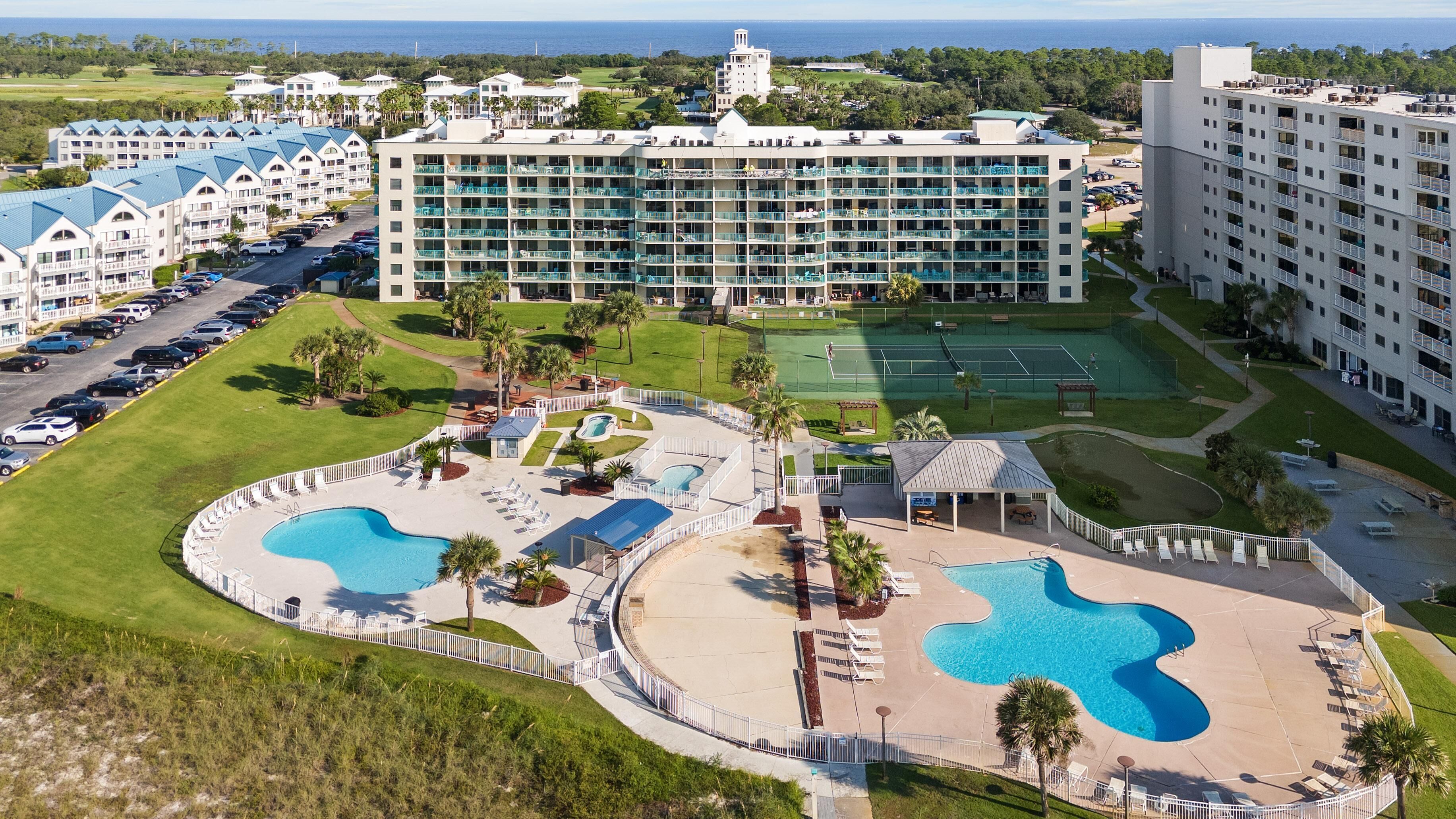 A resort with multiple swimming pools, a tennis court, and a large building with balconies.