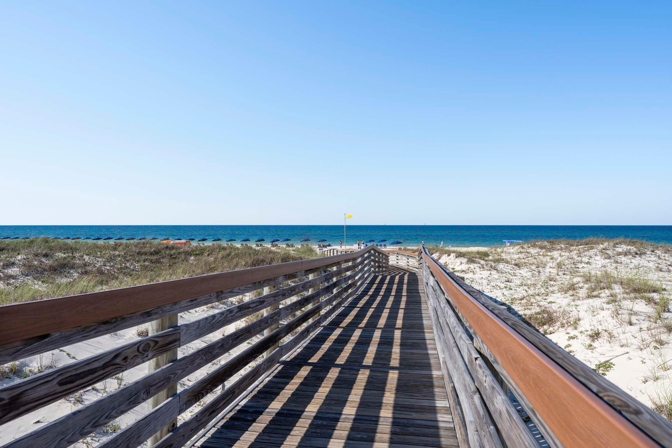A wooden boardwalk leading to a beach with a clear sky.