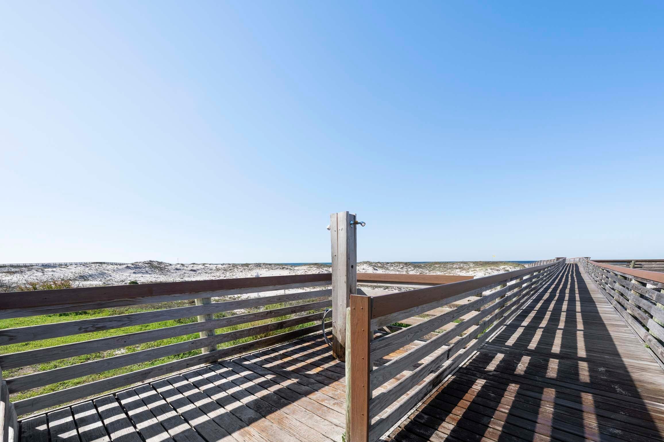A wooden boardwalk leading to a beach with a clear sky.