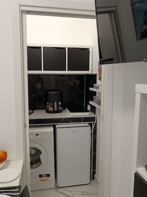 Eine kleine Küche mit Waschmaschine, kleinem Kühlschrank und Mikrowelle.