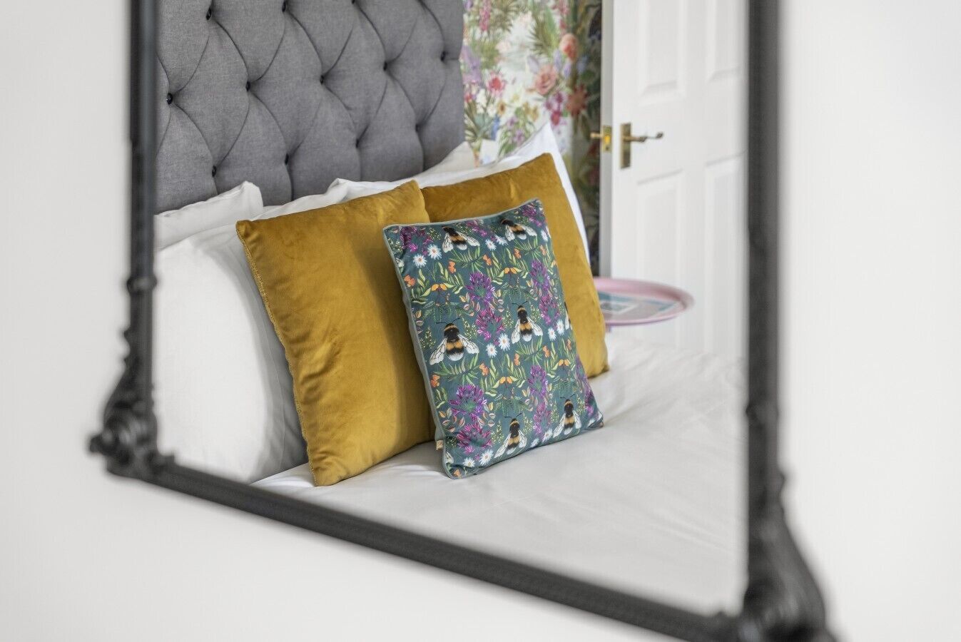 Een bed met een gestoffeerd hoofdbord, een mosterdkleurig kussen en een kussen met bloemenprint.