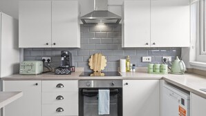 Una cuina moderna amb armaris blancs, una campana extractora d'acer inoxidable, forn integrat i una cafetera a la tauleta.