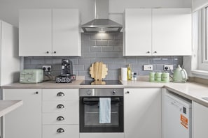 Une cuisine moderne avec des armoires blanches, une hotte de cuisinière en acier inoxydable, un four encastré et une machine à café posée sur le plan de travail.