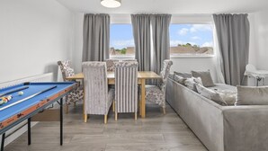Una habitació amb taula de billar, sofà, taula de menjador amb cadires i vistes per la finestra.