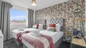 Habitació d'hotel amb dos llits, una finestra gran, un ventilador de sostre i un fons de pantalla tropical.