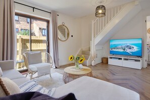 Un soggiorno con un divano, un tavolino rotondo con girasoli, una TV su un mobile bianco e una scala.