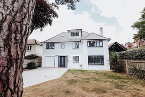 Une maison à deux étages avec un garage à l’avant, une porte d’entrée et un petit jardin devant, agrémenté d’un arbre et d’une clôture.