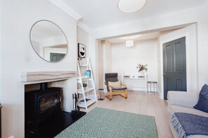 Una sala de estar con chimenea, un espejo redondo, un sofá, una silla, una mesita y una puerta.