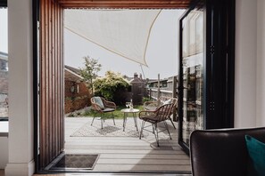 Un patio con sillas de mimbre, una pequeña mesa y un ventanal que da a un jardín.