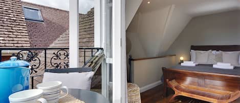 A bedroom with a wooden bed, a small window, and a balcony with a blue kettle and mugs.