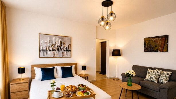 Ett modernt hotellrum med en säng i trä, ett brickbord med frukost, en soffa och konstverk på väggarna.