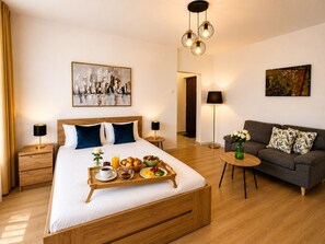A modern hotel room with a wooden bed, a breakfast tray, a sofa, and artwork on the walls. - Metropole Apartments Prime One (Bucharest)
