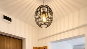 En modern inredning med en dörr i trä, en väggmonterad klädhängare, en grå soffa och en hängande lampa.