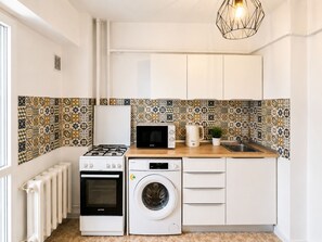A compact kitchen with a gas stove, microwave, oven, and washing machine. - Metropole Apartments Prime One (Bucharest)