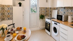 Ett modernt kök med vita skåp, ett matbord med frukost, en tvättmaskin och en mikrovågsugn.
