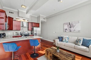 Eine moderne Küche mit Kochinsel, Barhocker, einem Esstisch und einer Wohnbereits mit Sofa und Zierkissen.