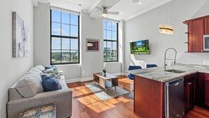 A modern kitchen with a built-in dishwasher, a dining area with a table and chairs, and large windows offering a city view. - Chic Modern 1BD | Northern Libs | Sleeps 2 Stay (Philadelphia)