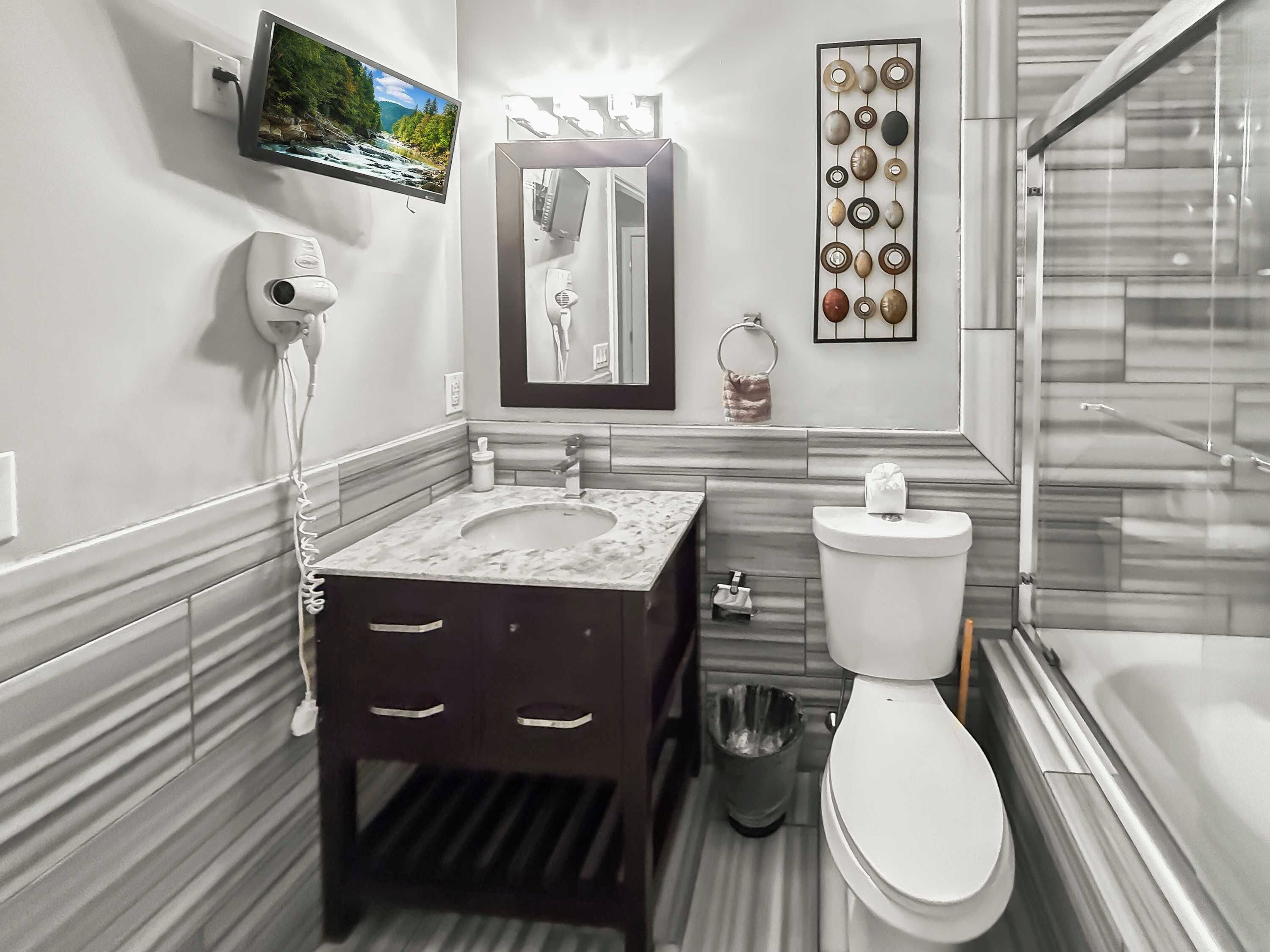 Casa de banho moderna com lavatório de mármore, sanita, secador de cabelo portátil, espelho e televisão na parede.