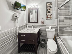 A modern bathroom with a marble sink, a toilet, a handheld hair dryer, a mirror, and a wall-mounted TV. - Sleek Studio near The Fillmore | NoLibs | Sleeps 2 (Philadelphia)