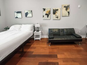 A bedroom with a bed, a nightstand, a lamp, a black sofa, and three abstract wall art pieces. - Sleek Studio near The Fillmore | NoLibs | Sleeps 2 (Philadelphia)