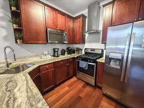 A kitchen with wooden cabinets, stainless steel appliances, a granite countertop, and a stainless steel refrigerator. - Sleek Studio near The Fillmore | NoLibs | Sleeps 2 (Philadelphia)