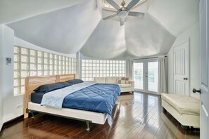 A bedroom with a bed, a sofa, a ceiling fan, and a large window with a view.