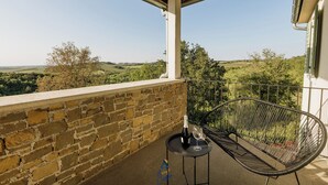 A balcony with a brick wall, a metal chair, a small round table with a bottle and glass, and a view of the countryside. - Villa Morgan – Luxury Villa with Heated Pool near Buje (Buje)