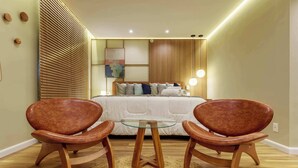 A bedroom with a bed, bedside tables, a glass coffee table, two leather chairs, a woven rug, and a wooden headboard. - #VD1226 | Cyclinn Berrini Chacara Sto Antonio (Berrini)