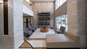A modern lobby with marble flooring, a central seating area with sofas, a bookshelf, and large windows. - #VD1226 | Cyclinn Berrini Chacara Sto Antonio (Berrini)