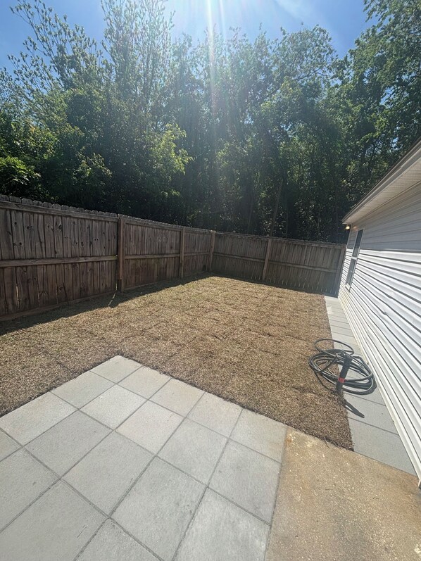A backyard with a wooden fence, a grassy area, and a tiled patio.