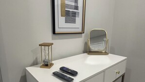 A white vanity with a gold-framed mirror, two remote controls, and a framed abstract artwork on the wall. - Delightful 2B/2B modern & Brand new centrally located (Florence)