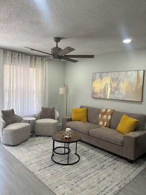 A modern living room with a ceiling fan, a sofa with cushions, a coffee table, and a floor lamp.