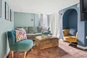 Ein Wohnzimmer mit einem petrolfarbenen Sofa, einem gelben Sessel, einem braunen Hocker und einer blauen Akzentwand.