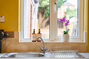 Ein Spülbecken mit Wasserhahn, ein Geschirrgestell und zwei Handseifenflaschen auf der Fensterbank.