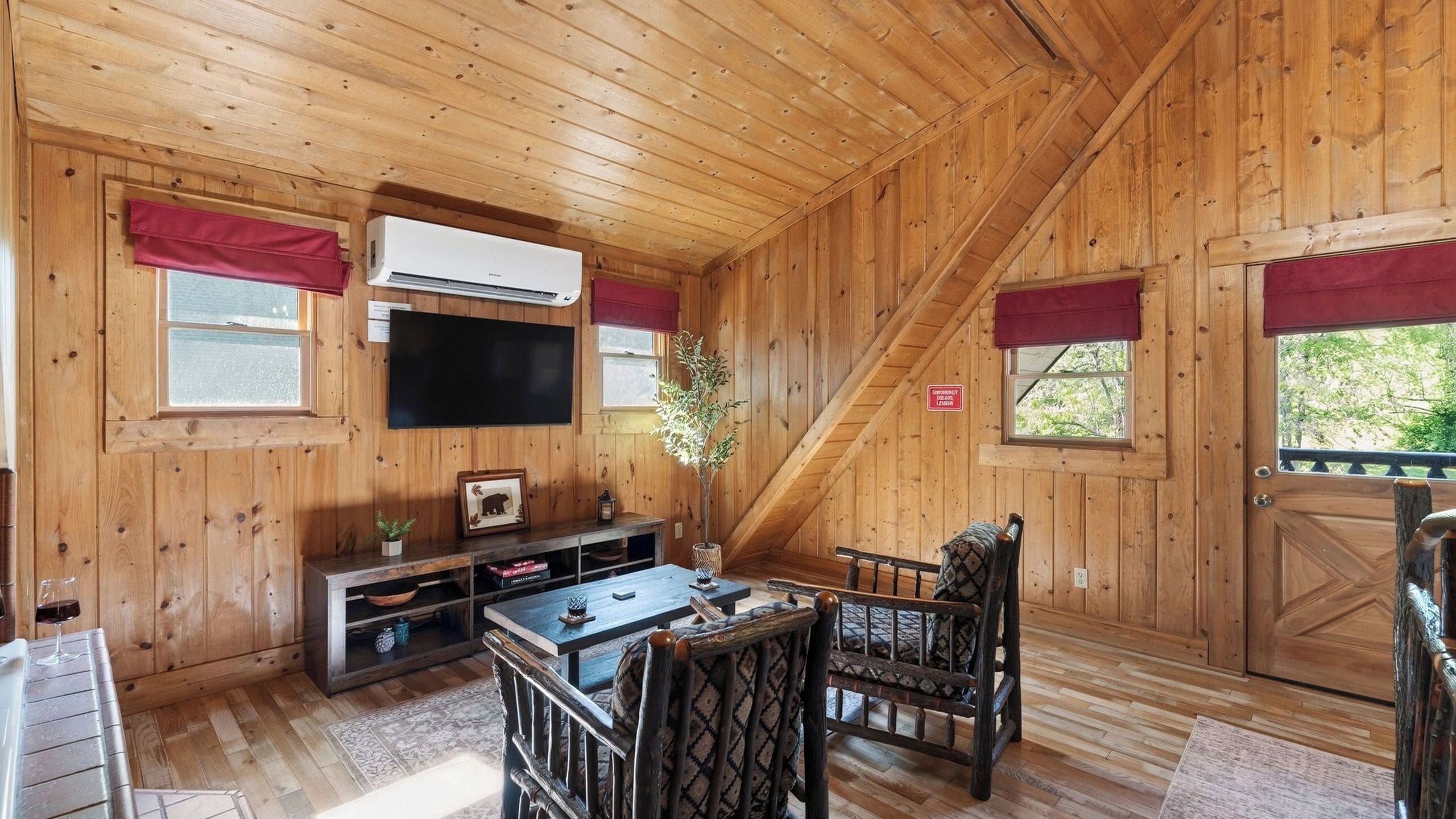 Ein Holzblockhaus-Interieur mit Fernseher, einem Esstisch, Stühlen, einem Kamin und einem Fenster mit Aussicht.