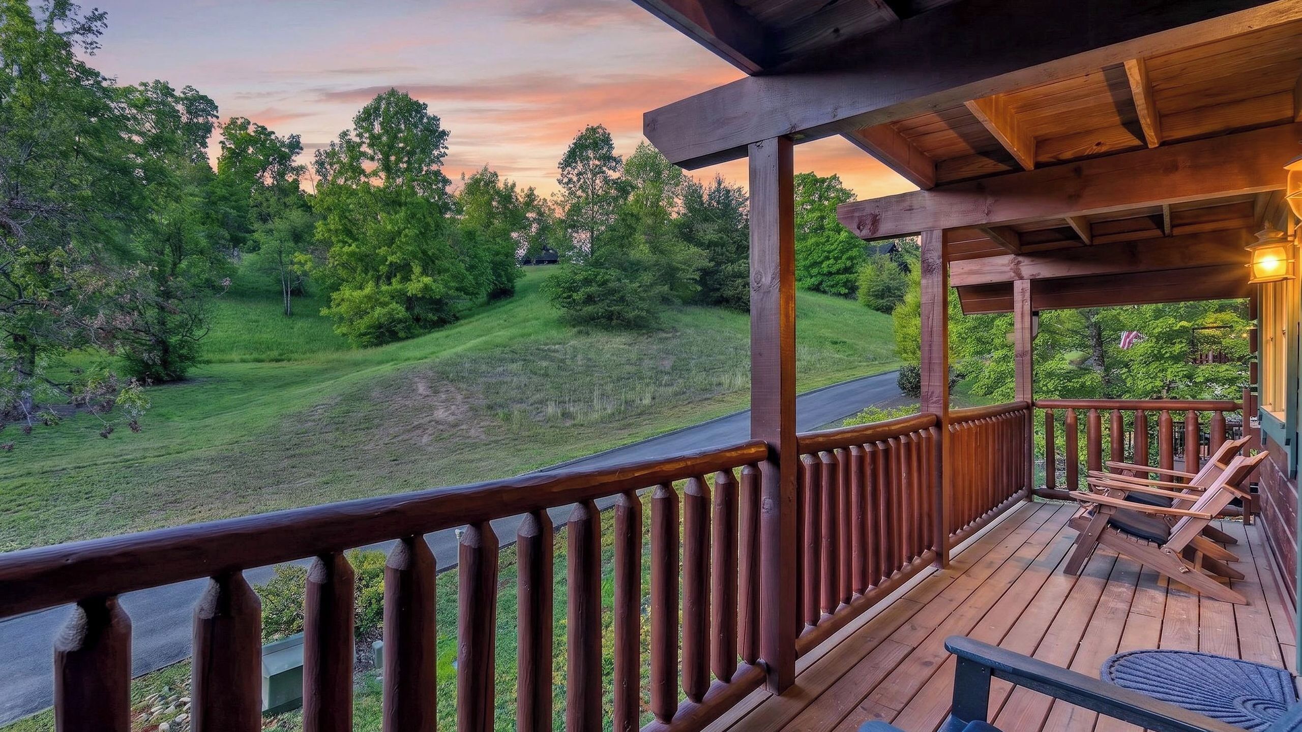 A wooden deck with a railing overlooking a grassy landscape and a road.