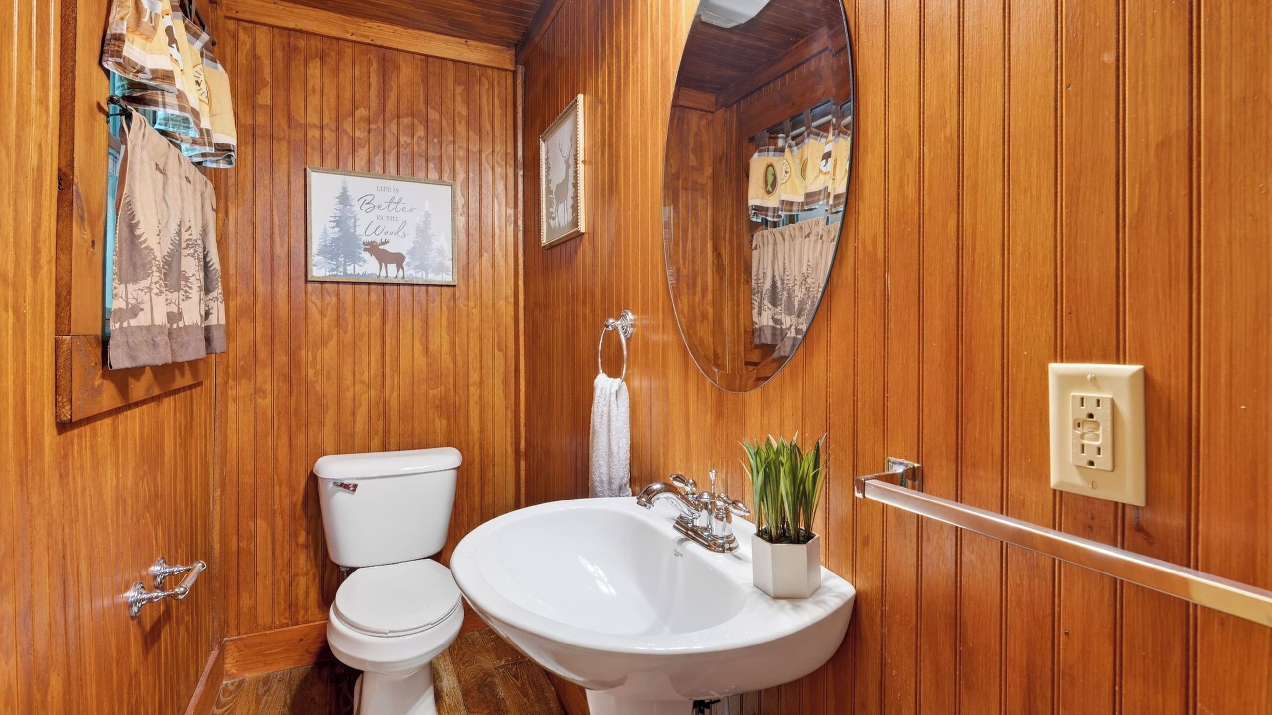A wooden-paneled bathroom with a toilet, sink, and a framed quote on the wall.