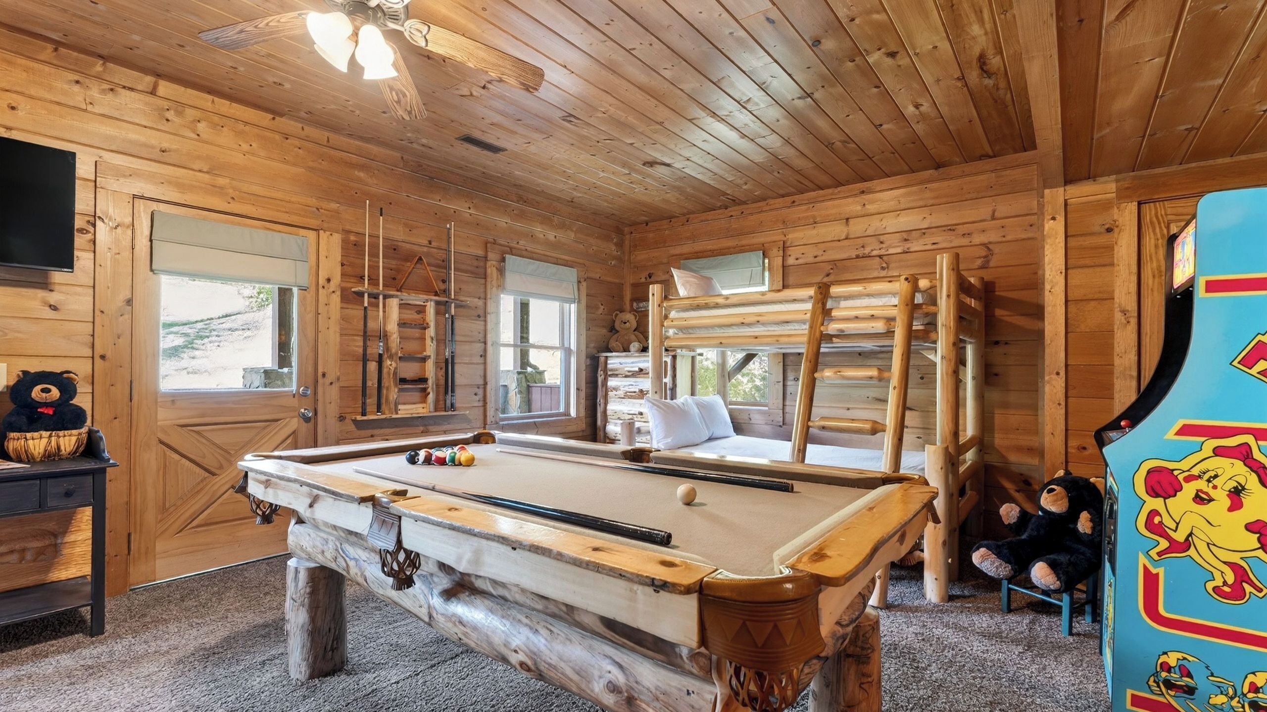 A wooden cabin interior with a pool table, a bed, and a bear-themed decoration.