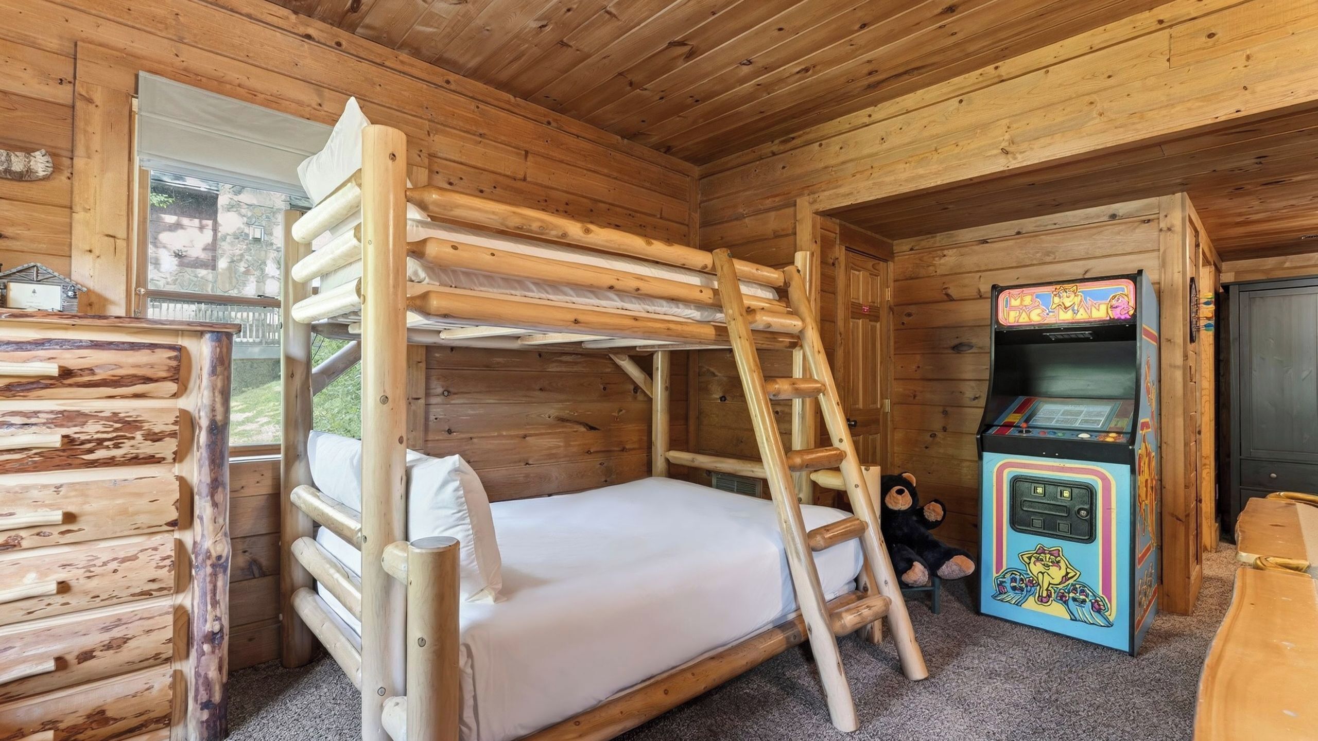 Una habitación de cabaña de madera con literas, una mesita pequeña y una máquina de videojuegos.