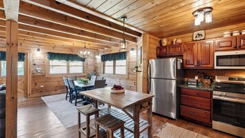 Interior de una cabaña de madera con una mesa de comedor, sillas, un refrigerador, un horno y armarios de madera.