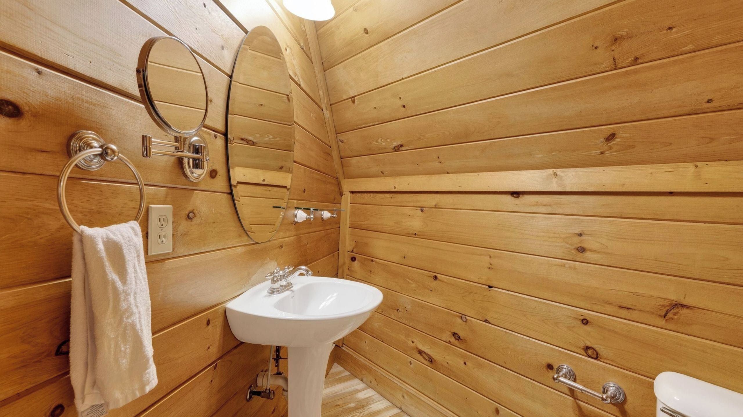 A wooden-paneled bathroom with a white sink, a mirror, a towel rack, and a toilet.