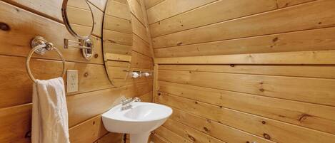 A wooden-paneled bathroom with a white sink, a mirror, a towel rack, and a toilet.