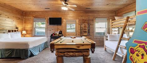 A wooden cabin room with a bed, a pool table, a TV, and a window.