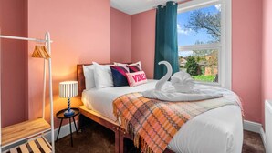 A bedroom with a bed, a bedside lamp, a window with a view, and a towel shaped like a swan. - Stylish 3BR Victorian House | Garden, BBQ, Parking (Worcestershire)
