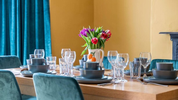 A dining table set with plates, bowls, and glasses, with a vase of flowers in the center. - Stylish 3BR Victorian House | Garden, BBQ, Parking (Worcestershire)