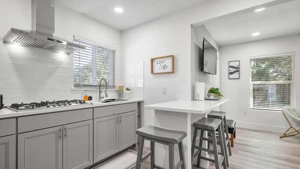 A modern kitchen with a gas stove, stainless steel range hood, and a white countertop.