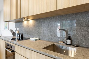 A modern kitchen with a granite countertop, stainless steel sink, wooden cabinets, and a built-in oven. - Modern apartment near the airport (Mangere Bridge)