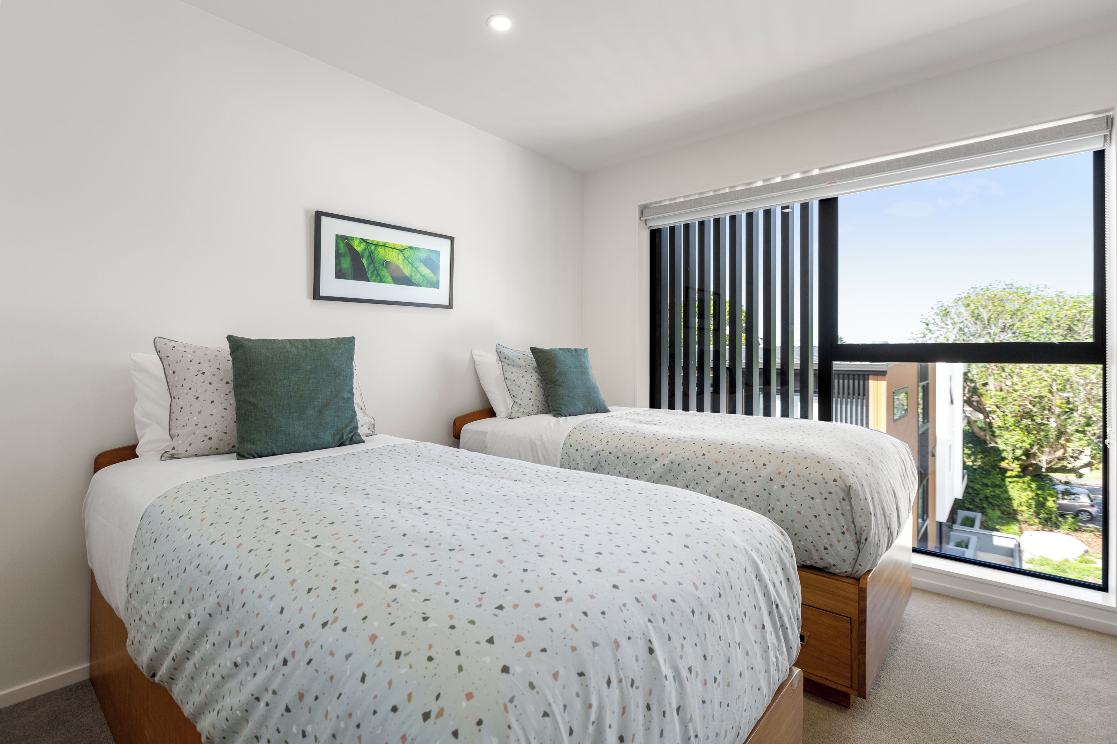 A bedroom with two beds, a window with blinds, and a framed picture on the wall.