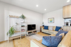 A living room with a TV, sofa, and bookshelf. - Modern apartment near the airport (Mangere Bridge)